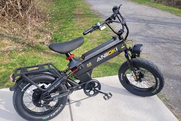 Aniioki A8 Pro Max black electric bike parked outdoors on a concrete pathway next to a grassy trail, illustrating the wheel and braking system for a guide on how to replace e-bike brake pads and rotors.