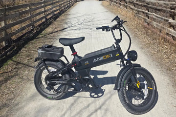 Black Aniioki A8 Pro Max long range ebike parked on a sunny gravel trail with wooden fences, demonstrating how long does ebike battery last during extended outdoor rides.